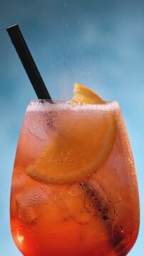 Glass of apperol spritz cocktail with orange slice and straw on blue background. Closeup of summer drink, zoom out