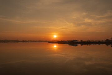 The sun is setting over a calm body of water, casting a warm glow over the scene