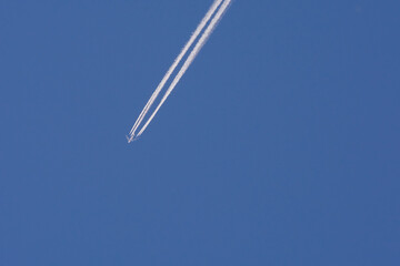 Bottom view of a passenger plane flying across the blue sky and leaving сontrails behind 