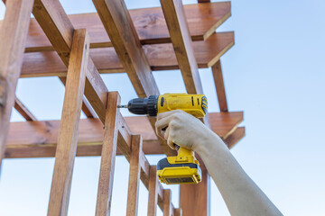 A woman assembles a wooden garden structure using a cordless drill, demonstrating home improvement...