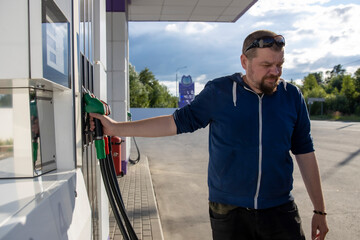 A man standing next to a gas pump filling up his vehicle with fuel at a gas station.