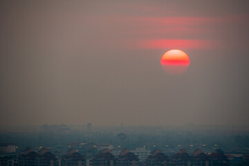 A red sun is setting over a city with a hazy atmosphere