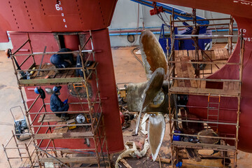 Cargo vessel in dry dock on ship repairing yard. Variable pitch propeller and rudder. Welder...