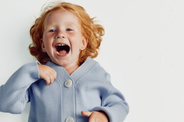 Funny redhaired girl in blue sweater making faces on white background for children's fashion and fun concept