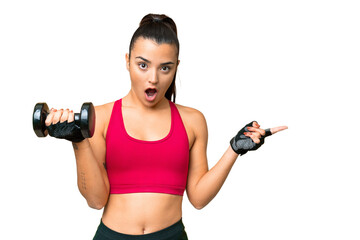 Young sport woman making weightlifting surprised and pointing side