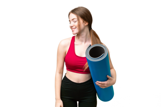 Young sport woman going to yoga classes while holding a mat over isolated chroma key background looking to the side and smiling