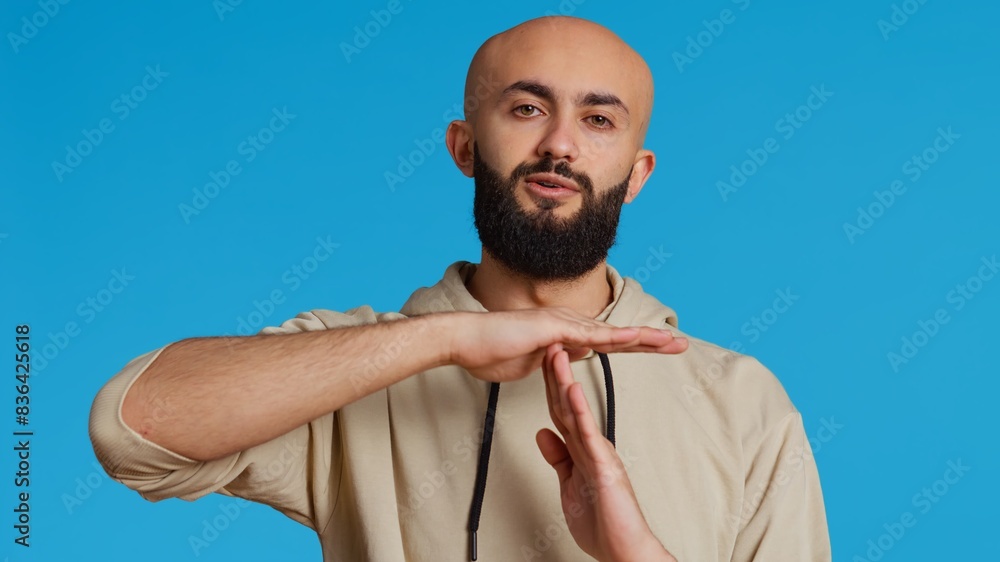 Poster middle eastern person doing timeout gesture on camera, asking for a break to stop working over blue 
