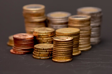 Stacks of euro cents coins of various denominations stacked on a black background, selective focus.