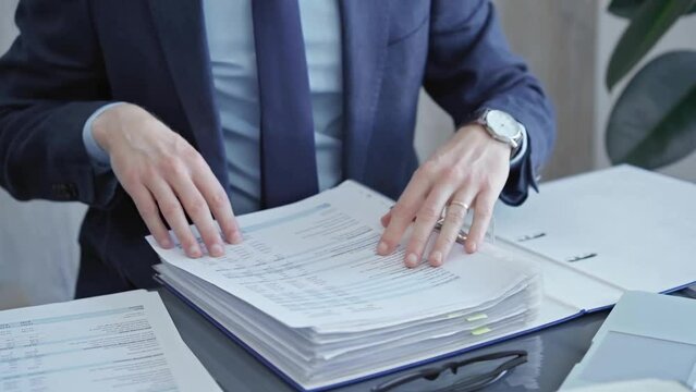 Professional auditor sorting through documents at desk. Close-up of a businessman or bookkeeper organizing paperwork in an office environment