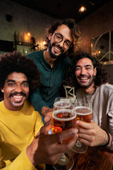 Vertical portrait of multiracial group of three men friends looking at camera while being in a bar...