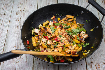Vegan pepper, tofu and zucchini stir fry in wok, wooden table,