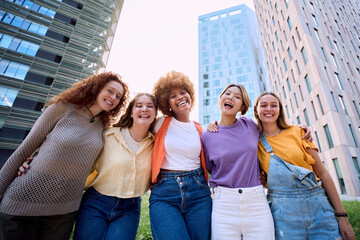 Multirracial cheerful young only women looking at camera together. This gathering cheerful female group portrait with skyscrapers at background having fun and laughing. Social gathering of diversity