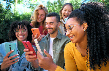 Obraz premium Group of smiling young friends using smart mobile phones app together. Millennials addicted to technology trends. University students and Social media online community. Focus on the Latina woman
