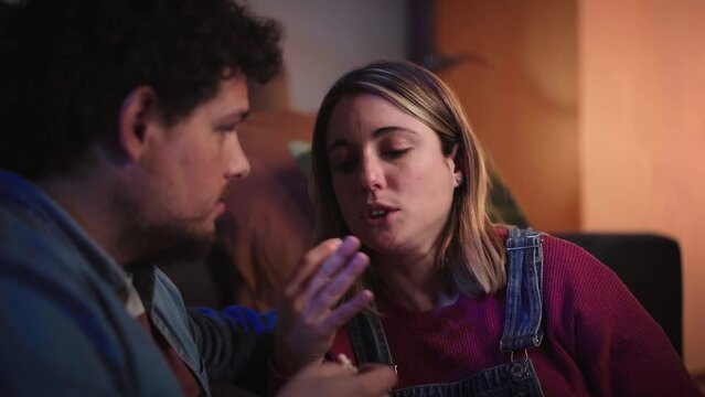 Young millennial couple chatting quiet sitting on living room sofa in evening. Calm Caucasian man and relaxed blonde woman eating popcorn talking together at home. Positive relationship in family