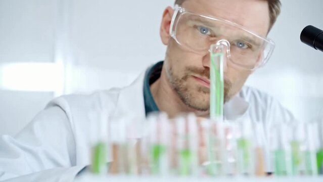 Man researcher with safety glasses is examining lab tube with a green fluid in a modern laboratory, close-up. Science, microbiology and medicine