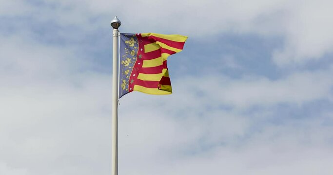 Slow motion footage of the Valencian Community flag waving in the wind on a clear day. The Valencian Community is an autonomous community of Spain