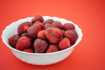 Fresh and ripe strawberries in a white bowl on red background