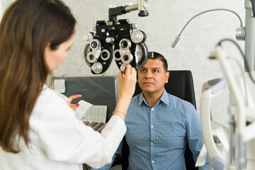 Concentrated eye doctor using a phoropter to assess the vision of a male patient in a contemporary...