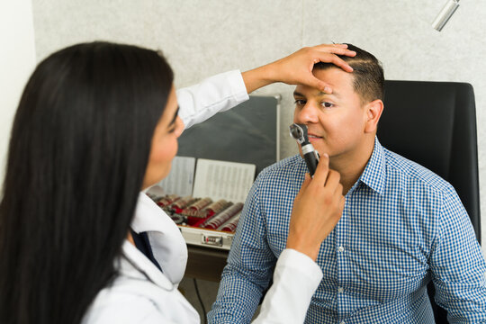Female ophthalmologist carefully inspects a male patient's eyes with an ottoscope during a regular medical examination