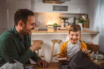 Young boy pack his notebook and book with dad for school in backpack