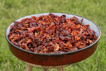 A full red casserole of red dried chili peppers that show off the texture and concept of the spice ingredients. The pan is placed on a wooden stool that has three legs.