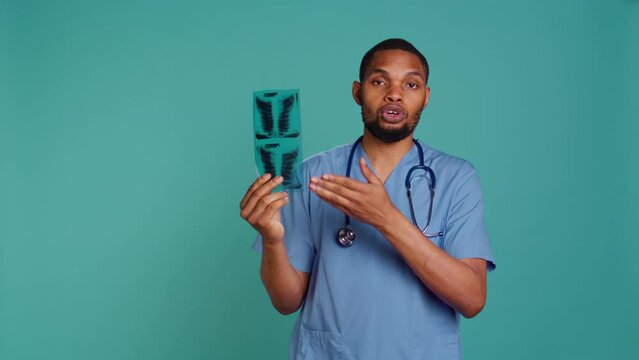 Healthcare professional informing patient of radiology x ray scan results, studio backdrop. African american doctor presenting radiography and providing injury treatment, camera B