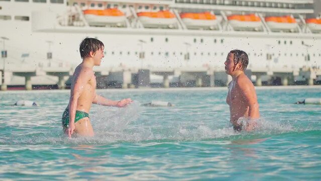4k, A view of two boys children splashing, playing in water, in the background cruise ship, Sir Bani Yas, United Arab Emirates