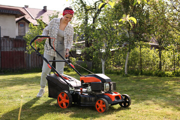 Smiling woman cutting green grass with lawn mower in garden