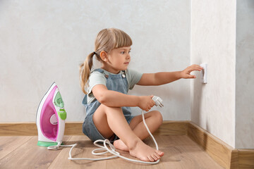 Little child playing with electrical socket and iron plug at home. Dangerous situation