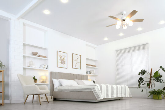 Comfortable furniture, ceiling fan, houseplants and accessories in stylish bedroom, low angle view