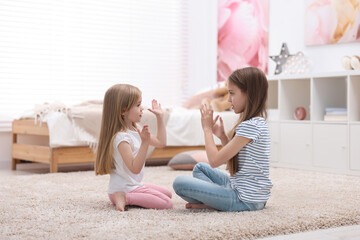 Cute little sisters playing clapping game with hands at home