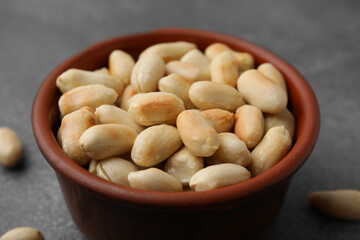 Roasted peanuts in bowl on brown table, closeup