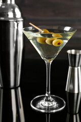 Metal shaker, Martini cocktail and jigger on black mirror surface