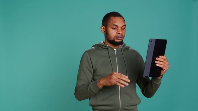 Angry man fighting with friend during videocall on tablet, isolated over studio background. Rude person in disagreement with mate, swearing and pointing finger in teleconference meeting, camera B