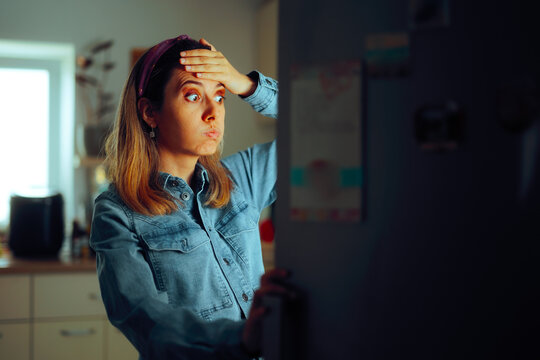 Woman looking Puzzled into the Fridge Wondering What to Eat. Girl checking the refrigerator remembering she forgot to buy something 
