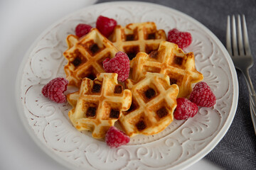 Tasty waffles with raspberries on a plate, top view.