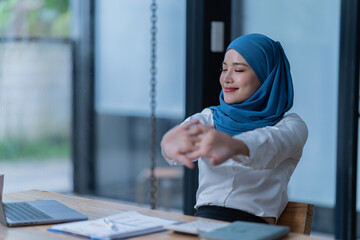 Cheerful muslim lady wear hijab working in the office, using laptop, Side view of smiling arab...