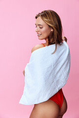 Vibrant woman in red swimsuit posing with towel on pink backdrop in summer beach theme