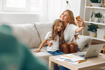 Mother and daughter shopping online together on a cozy couch, holding a credit card and using a laptop