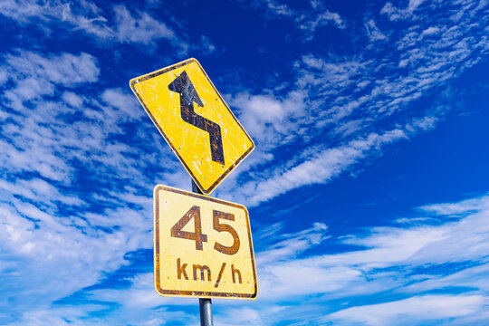 Yellow winding road warning sign with blue sky background