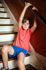Portrait of a young boy sitting on stairs casually hanging on to the railing