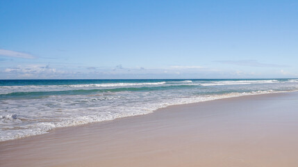Panoramic beach scene with wet smooth sand, sea, breaking waves, horizon and blue sky and copyspace, blank space with no landmarks, nobody, no people
