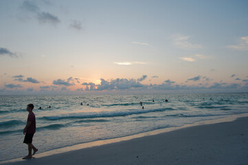 Sunset at Pass-a-grille Beach in St Petersburg Florida. Low light with multiple people in the water. Golden glow and blue sky of the Sun in the background. Horizontal View. Cloudscape landscape.
