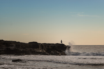 Fisherman on a small headland with waves crashing into the rocks.