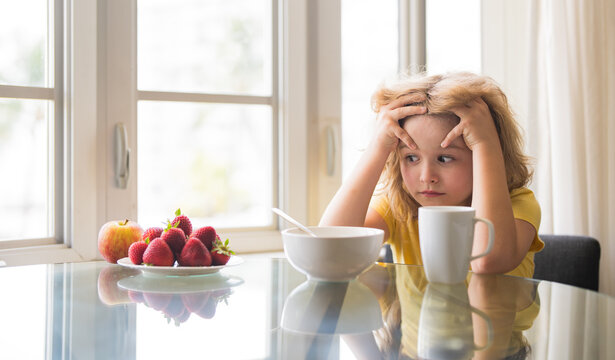 Unhappy little boy child sit at table at home kitchen have no appetite for healthy breakfast. Upset kid refuse to eat cereals with milk. Adorable sad tired kid eating low fat soy milk in bowl cereal. - Powered by Adobe