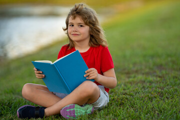 Smart child boy reading book in park outdoor. Blonde kid reading a book in summer. Clever kids...