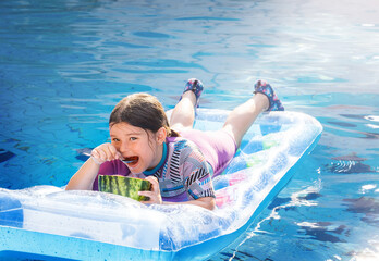 Portrait of a happy child on an air mattress eating a watermelon