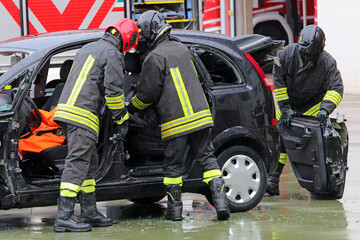firefighters unhinging the stuck door of a crashed car after the collision to free the injured...