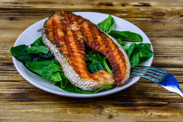 Plate with roasted salmon steak and spinach leaves on a wooden table