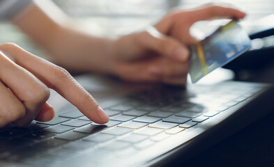 Close-up of hand holding credit card and type on laptop keyboard with online payment for shopping.